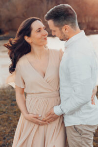 Schwangere Mama streichelt liebevoll ihren Bauch und schaut ihren Mann an, der auch den Bauch streichelt. Babybauchfotos Würzburg